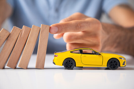 Male hand stopping wooden blocks from falling on toy car.