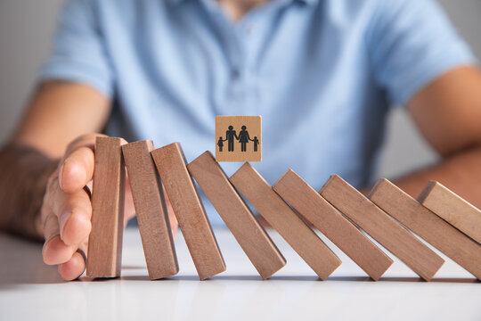 Male hand stopping wooden blocks from falling on family.