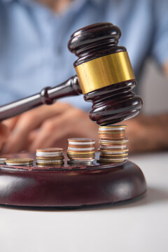 Male hand showing judge gavel over coins.