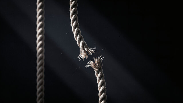 Frayed rope snapped apart under tension against a dark background breaking point, concept
