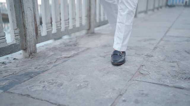 Close up of groom or man legs walking forward wearing elegant white pants and formal leather shoes