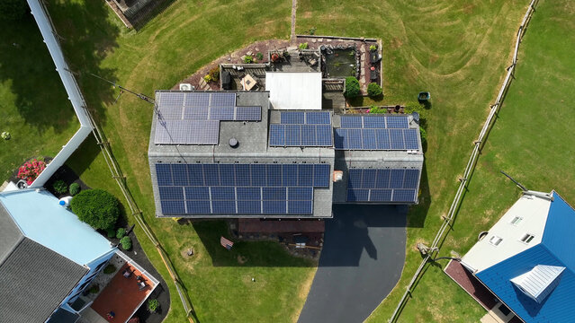 Aerial view of a residential house featuring a roof covered in solar panels, surrounded by a green lawn and a paved driveway in Willow Street, Pennsylvania, United States.