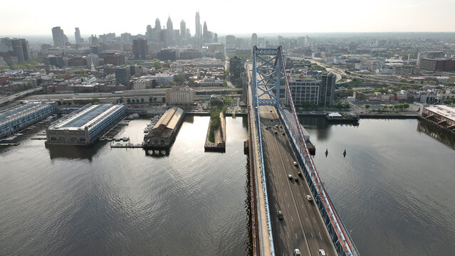 Aerial view of the Benjamin Franklin Bridge spanning the Delaware River with the Philadelphia skyline, historic piers, and urban infrastructure in Philadelphia, Pennsylvania, United States.