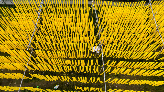 Aerial view of yellow fabric strips hanging to dry on bamboo frames in an open field in Narayanganj, Dhaka Division, Bangladesh.