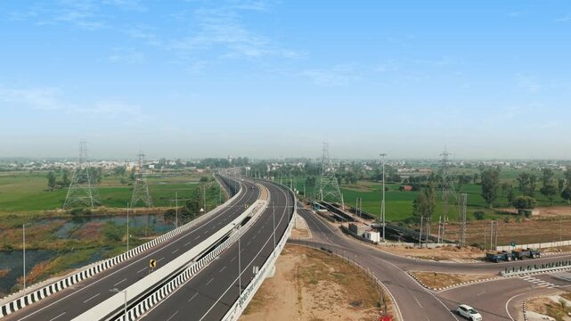 Cinematic 4K aerial footage showcasing modern highway infrastructure crossing the rural landscape of Haryana, with green farmland, curved roadways, power lines, and surrounding villages.