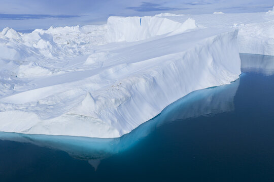 Aerial view of a massive white iceberg floating in the deep blue waters of the Ilulissat Icefjord, showcasing the dramatic arctic landscape of Ilulissat, Avannaata Municipalit, Greenland.