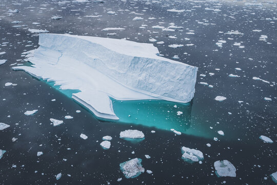 Aerial view of a massive iceberg floating in the turquoise waters of the Ilulissat Icefjord surrounded by scattered ice fragments in Ilulissat, Avannaata Kommunia, Greenland.