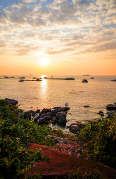 Sunset over sea with floating fish farms and two people standing on rocky shore, golden light reflecting on water. Path to sea at sunset. Vietnam, Phu Quoc