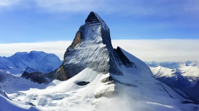 Snow-covered pyramidal mountain slowly grows larger in frame as pale mist drifts across glacier-covered lower slopes beneath clear blue sky and layered distant peaks