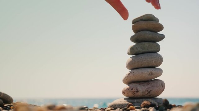 Zen rock balancing on beach shore with calm sea background.