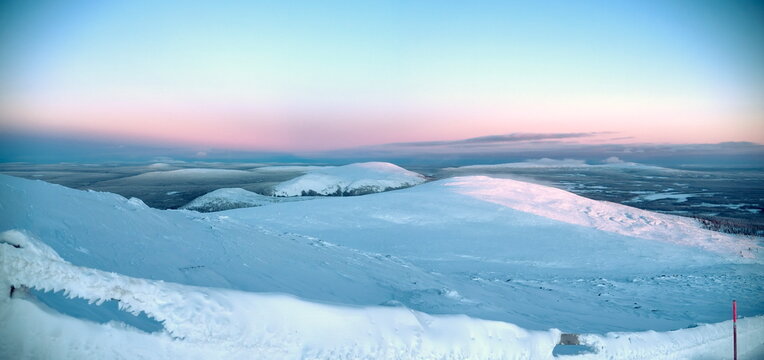 Kolari, Finland - 26.12.2018: Vast snow-covered hills under a soft pink and blue twilight sky in the Lapland wilderness