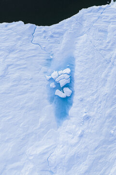 Aerial view of a massive iceberg with a bright blue meltwater pool and fractured ice blocks in the Ilulissat Icefjord, Ilulissat, Avannaata Municipalit, Greenland.
