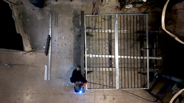 Overhead view of a welder tack welding a steel gate frame seen from above