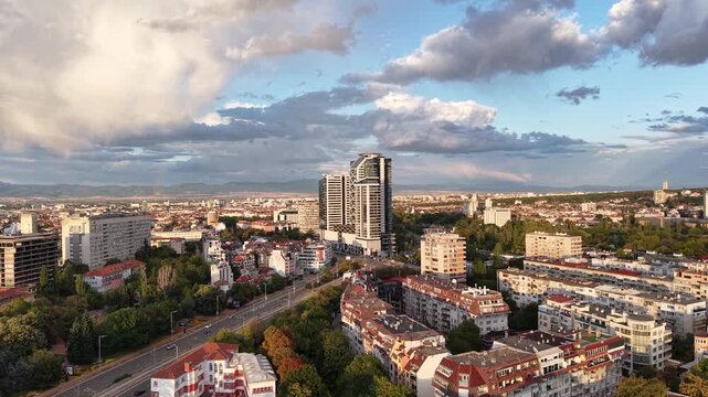 Modern high-rise towers dominate an urban skyline as a drone moves forward across a dense city district.