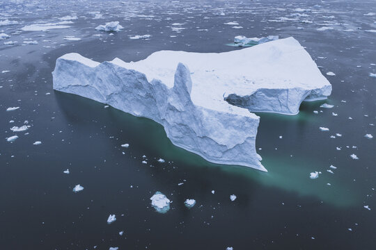 Aerial view of a massive iceberg floating in the deep blue waters of the Ilulissat Icefjord surrounded by scattered ice fragments in Ilulissat, Avannaata Municipalit, Greenland.