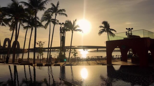 Cinematic moving pan shot of an infinity pool reflecting palm trees against a golden sunset in Phu Quoc Vietnam