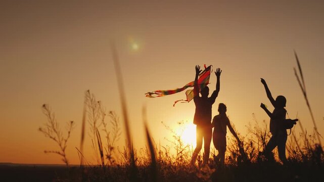 Happy family playing with kite together during golden hour sunset in field.