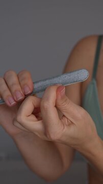 Young woman filing fingernails with gray nail file, close-up of hands during manicure, nail shaping, cuticle care and home beauty routine on gray background