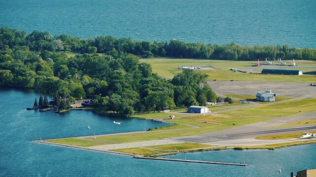 Aerial view of small airport runway adjacent to lush green island and blue water.