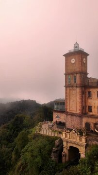 Moody, vertical view of the detailed French Village clock tower at Ba Na Hills, Da Nang, Vietnam, perched above a misty forested mountain slope