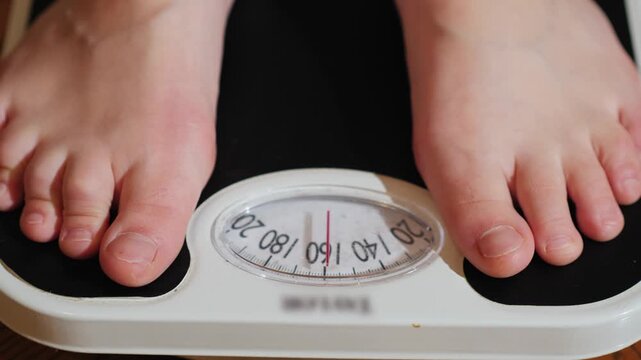 A close up view of person stepping on bathroom scales showing weight on measurement display.