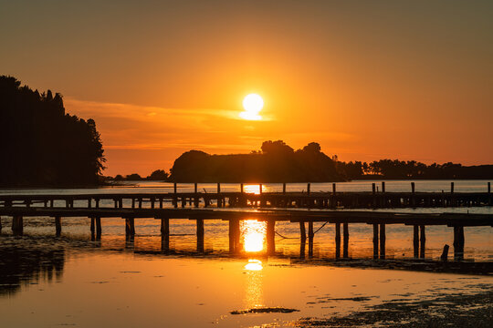 Seaside landscape near the city of Vlore in Albania, Europe. Breathtaking sunset over a tranquil lake with wooden piers and silhouette trees casting golden reflections on the water