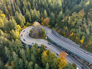 Naklejka premium Aerial view of a hairpin mountain road curve with a cross on rock in autumn