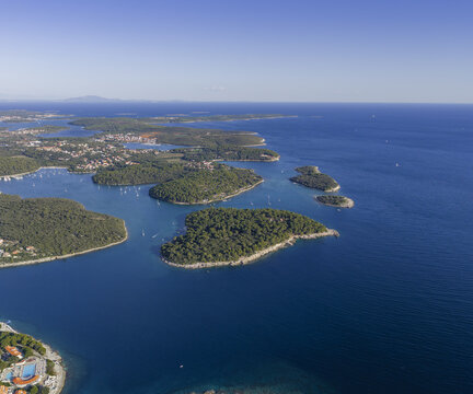 Aerial view of the coastline of Pjescana Uvala, featuring lush green islands, clear blue Adriatic Sea, and scattered sailboats in Pula, Istarska zupanija, Croatia.