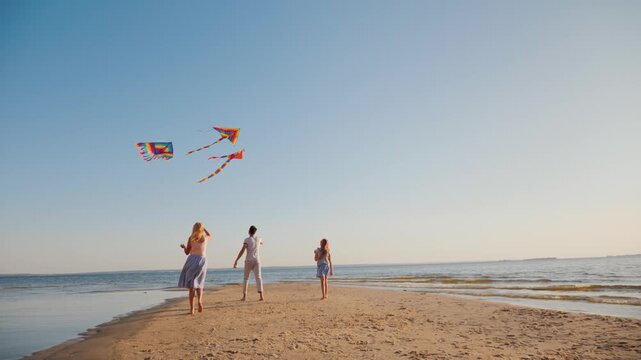 Happy family flying kites together on sandy beach during golden hour sunset at seaside.