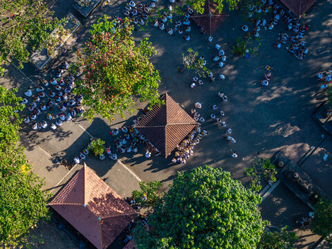 Aerial view of the Ngelarung Sea Offering Ceremony at Pura Segara Goa Lawah with people in traditional white clothing gathered around temple pavilions in Dawan, Bali, Indonesia.