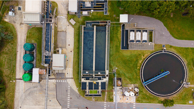 Aerial view of the wastewater treatment plant featuring circular sedimentation tanks, rectangular filtration basins, and green storage silos in Rancate, Lombardia, Italy.
