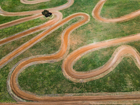 Aerial view of a winding dirt motocross track cutting through a vibrant green grassy field in Woorinen North, Victoria, Australia.