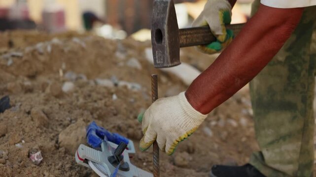 Worker hammering metal stake into ground at construction site