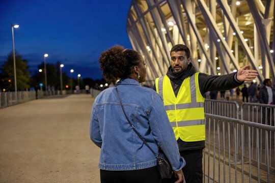 Sports venue crowd safety marshal directing an attendee into a transit lane