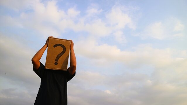 Person wearing a cardboard box with a question mark over their head against a cloudy sky.
