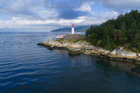 Aerial view of Point Atkinson Lighthouse situated on a rocky headland surrounded by evergreen trees and the Pacific Ocean under a cloudy sky in West Vancouver, British Columbia, Canada.