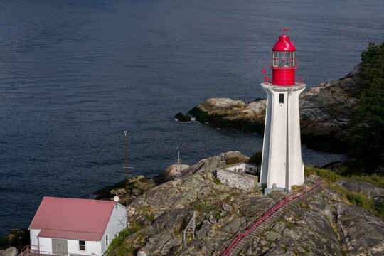 Aerial view of Point Atkinson Lighthouse with its red lantern room and white tower, on a rocky coastline overlooking the Pacific Ocean in West Vancouver, British Columbia, Canada.