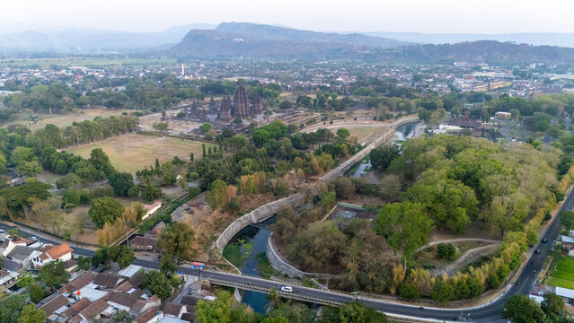 Aerial view of Prambanan Temple surrounded by lush greenery, a winding river, and a bridge in the foreground in Kecamatan Prambanan, Daerah Istimewa Yogya, Indonesia.