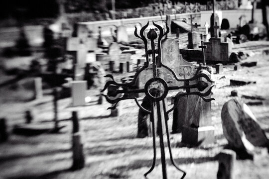 Old iron cross in cemetery. Black and white image. Selective focus, tilt shift, partly blurred. Ancient tombstone detail.