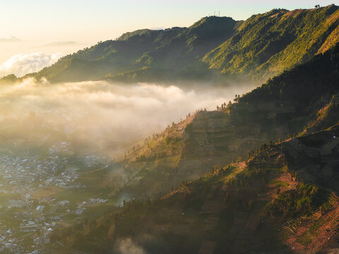 Aerial view of Dieng Plateau with terraced fields and a village nestled in the mountains under golden hour light in Indonesia.