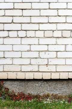 Old cracked white brick wall with green grass. Architectural detail background.