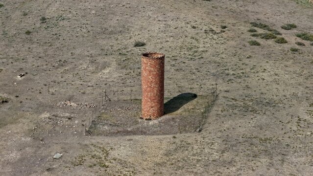 Aerial view of a historic brick chimney standing in a dry, grassy field surrounded by a wire fence in Golden, Colorado, United States.