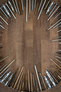 Circle made of various screws and nails on brown wood texture. Industrial flat lay. Carpentry still life.