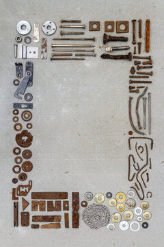 A frame of various old rusty bits and pieces arranged on a concrete surface. Old rusty nuts, bolts, nails and other parts flay lay on gray background.