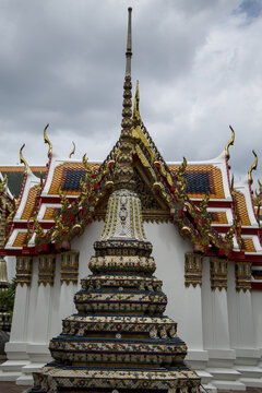 Vertical perspective of ornate mosaic stupa tower rising above colorful multi tiered tiled temple roofs at Wat Pho in Bangkok, Thailand.
