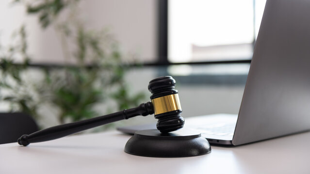 Judge gavel and laptop on an office desk with blurred plants, representing digital justice, online law, legal technology, court services, regulation, compliance, and professional legal work.