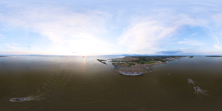 Aerial view of a large sailing ship docked at a pier with small boats navigating the calm coastal waters during a golden sunset in Metro Vancouver A, British Columbia, Canada.