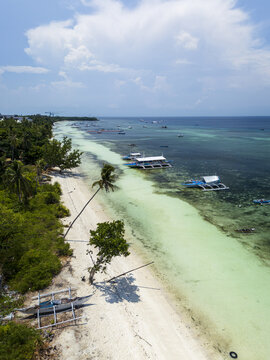 Aerial view of Doljo Beach with traditional outrigger boats anchored in turquoise waters along the white sandy coastline in Panglao, Central Visayas, Philippines.