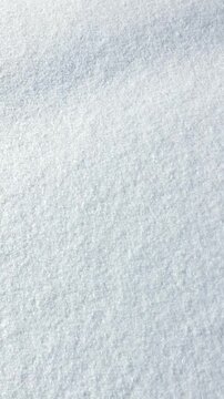 Fresh white snow creating smooth solid texture glowing in winter sunlight; vertical video capturing movement from left to right; abstract monochrome seasonal background evoking feeling of purity, joy 