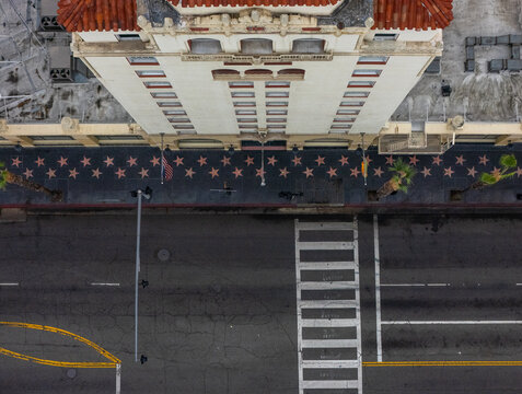 Aerial view of the Hollywood Walk of Fame with its iconic stars embedded in the sidewalk, adjacent to a historic building facade and a crosswalk in Los Angeles, California, United States.